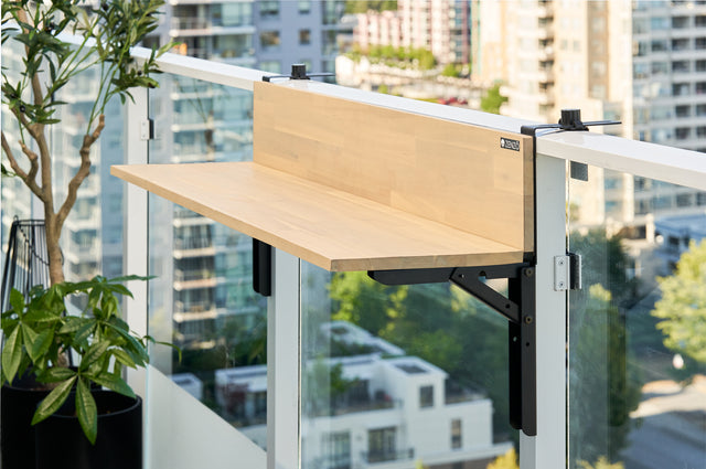 Zenzo Balcony Bar in birch wood finish installed on a glass balcony railing. The bar is empty, showcasing its sleek design with a scenic city view and greenery in the background.